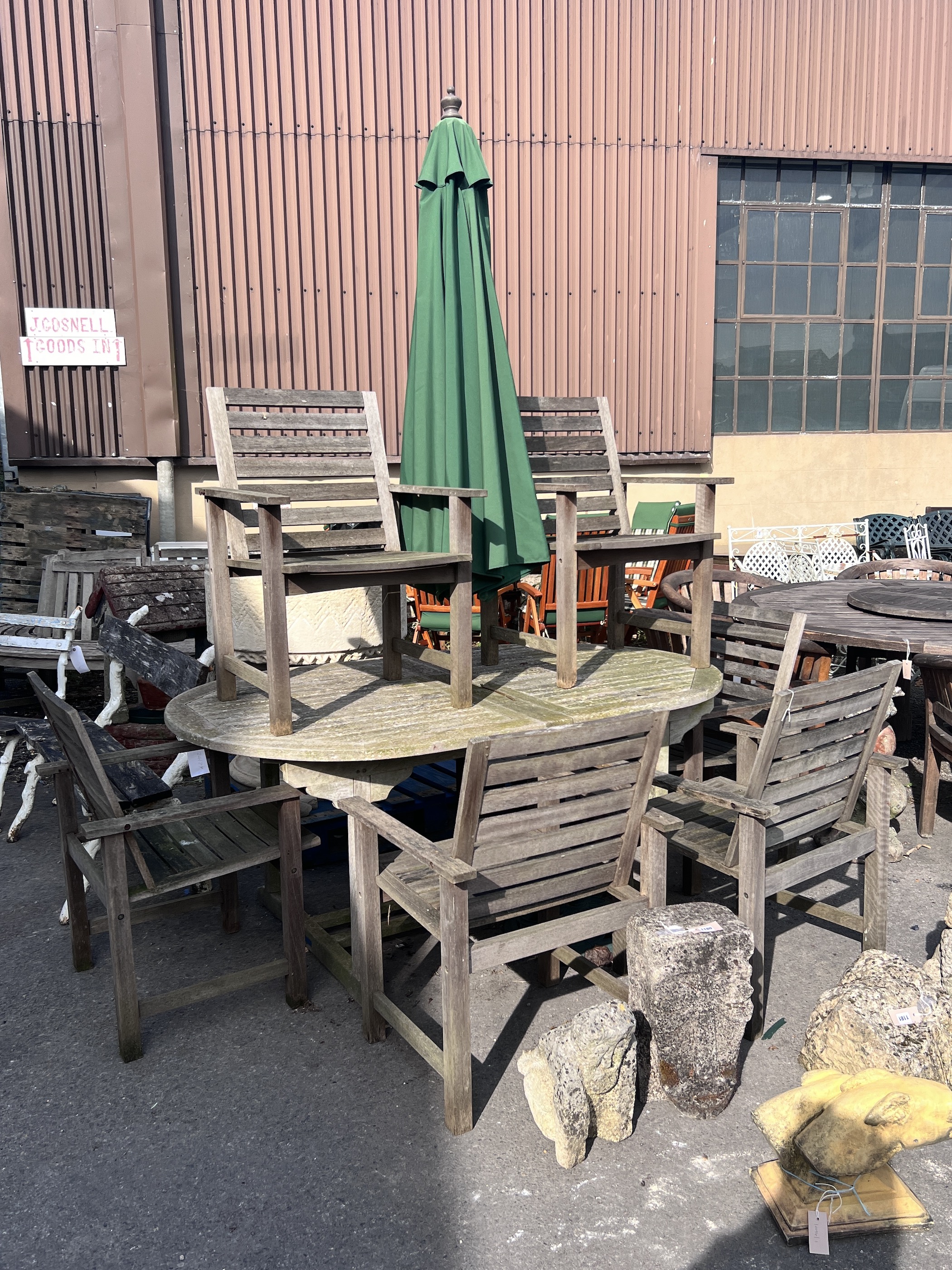 A weathered teak extending garden table, length 180cm, depth 110cm, height 76cm, together with six teak garden elbow chairs and a green canvas parasol